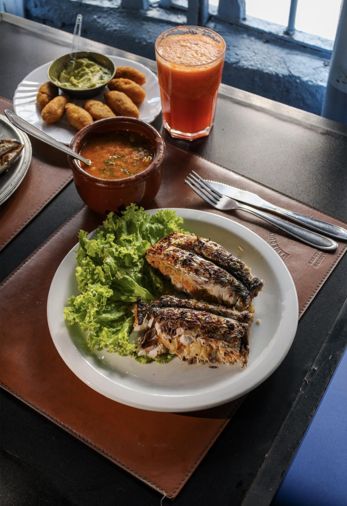 Prato de peixe grelhado com salada, bolinhos e suco servido no restaurante